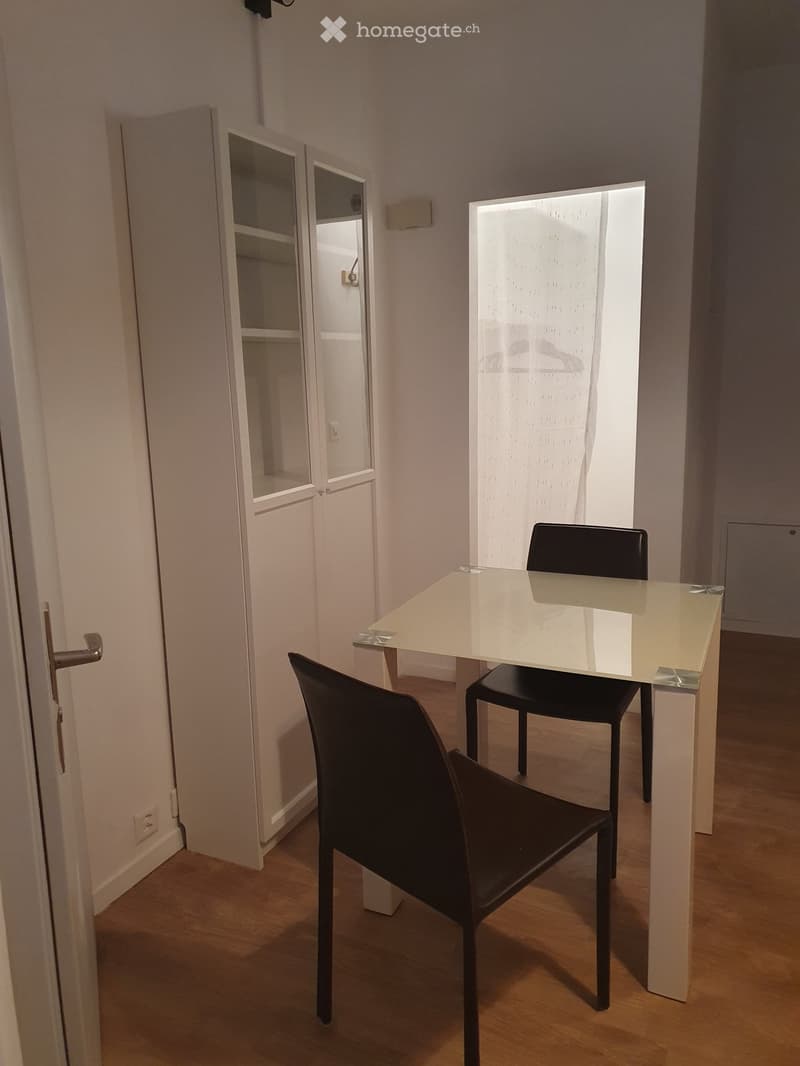 A small, modern dining area with a glass table and two black chairs, adjacent to a closet with mirrored doors.