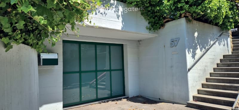 Modern white building entrance with green-framed glass door, number 57, and a raised ground floor accessed by concrete stairs.