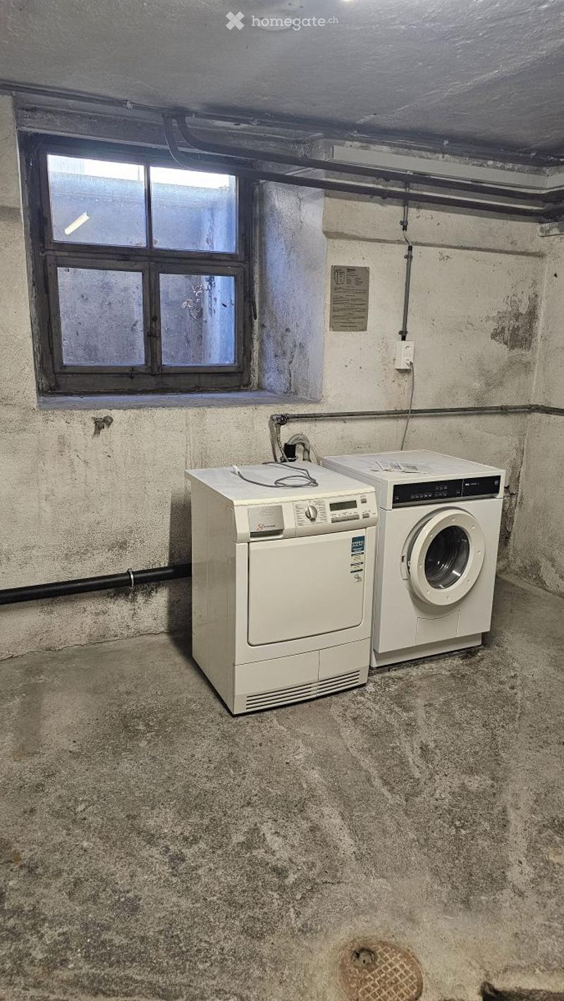 Concrete-walled room with a window, containing a washing machine and dryer.