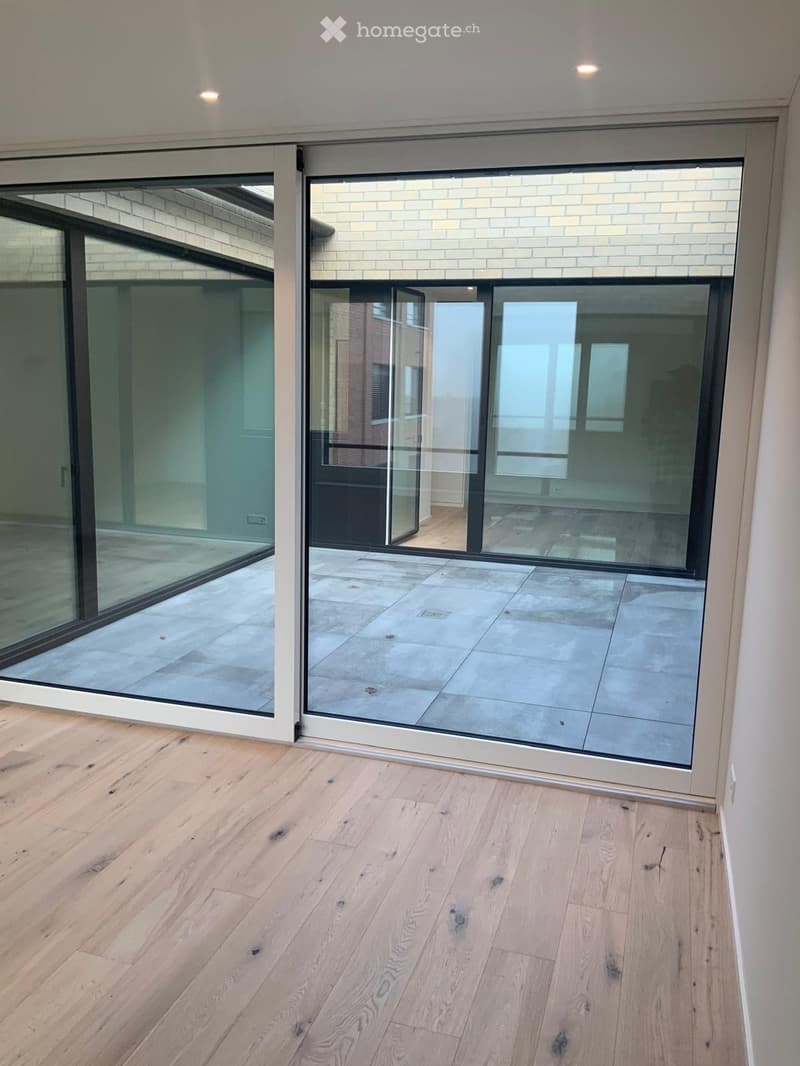 Empty room with light wooden flooring and large glass sliding doors leading to a tiled outdoor area.