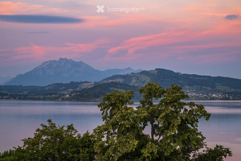 A scenic view of a lake surrounded by lush green trees and distant mountains under a colorful sunset sky.