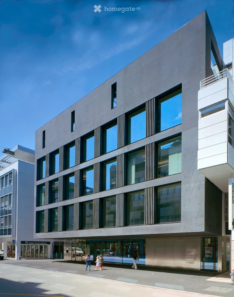 Modern multi-story building with large glass windows and a sleek concrete facade, located on a city street with pedestrians nearby.