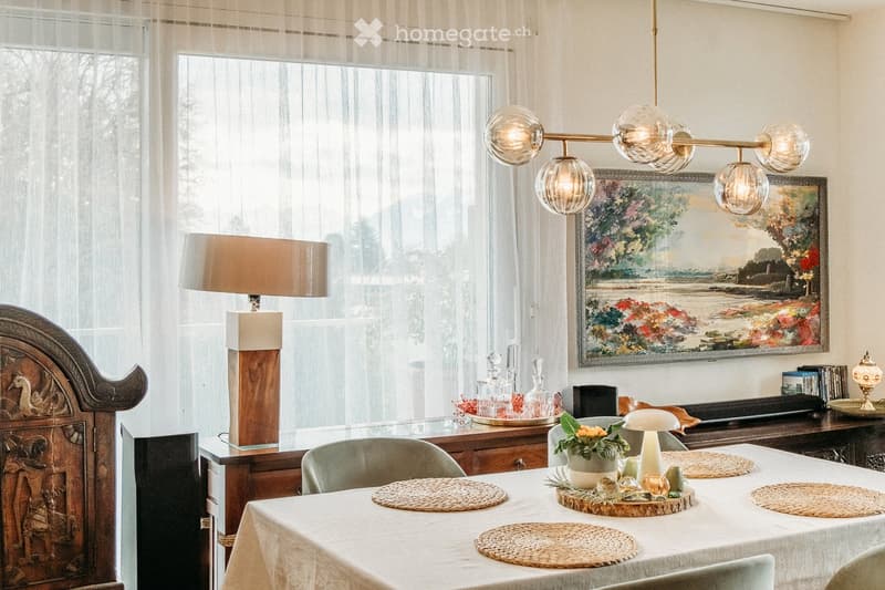 Dining room with a white tablecloth-covered table, six chairs, a floor lamp, a cabinet, and a painting on the wall.