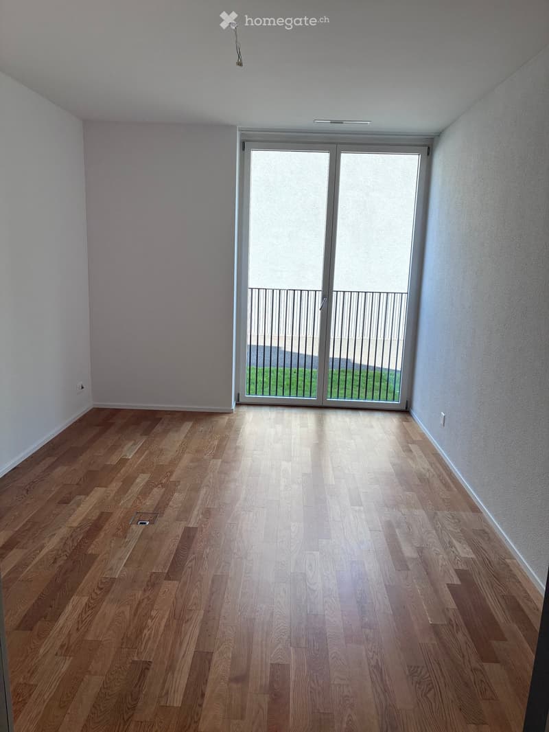 Empty room with wooden flooring, white walls, and a large sliding glass door leading to a balcony with a metal railing.