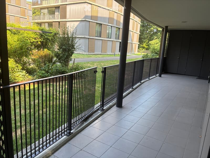 Balcony with tiled floor, metal railing, and view of greenery and modern building.