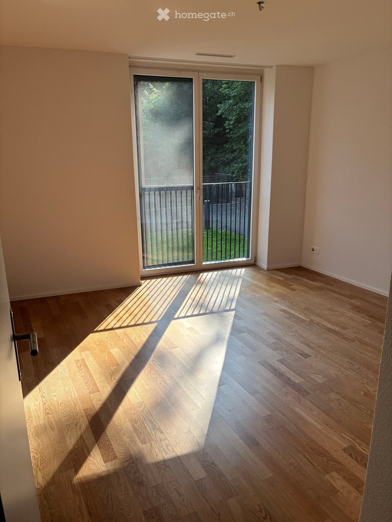 Empty room with light wooden flooring and large sliding glass doors leading to a balcony area.