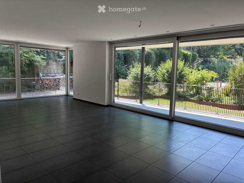 Empty room with large sliding glass doors leading to a garden, tiled floor, and modern ceiling lights.