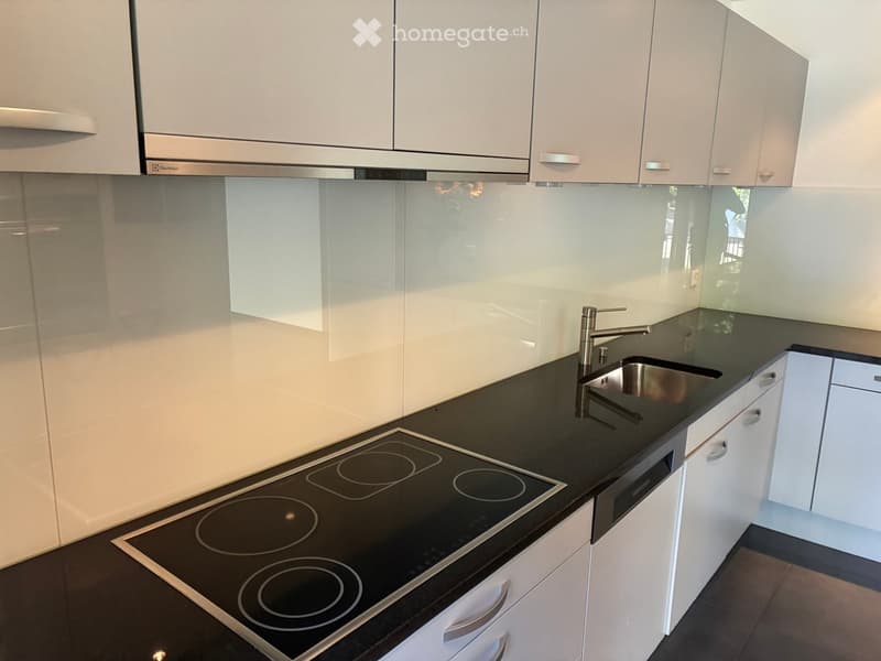 Modern kitchen with white cabinets, black countertops, an induction cooktop, and a stainless steel sink with a modern faucet.