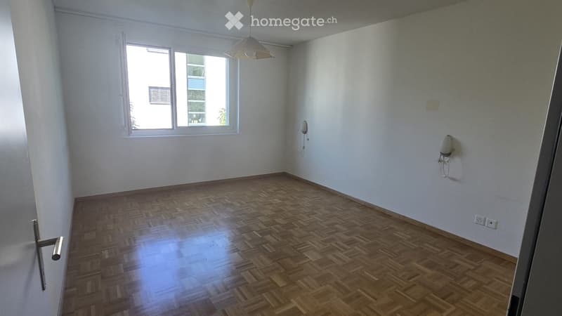 Empty room with wooden parquet flooring, white walls, and a single window with white frame. No furniture or equipment present.