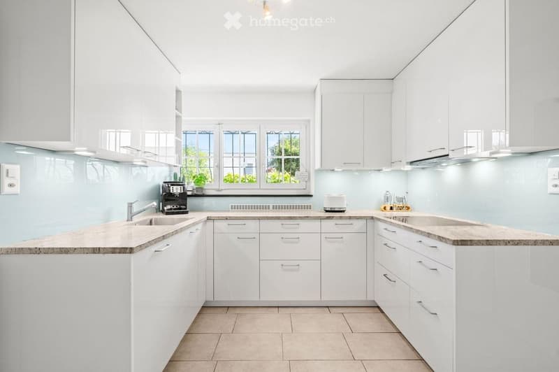 Modern kitchen with white cabinets, granite countertops, and stainless steel appliances. Features a large window with a view of greenery, a sink with a modern faucet, and a coffee maker on the counter.