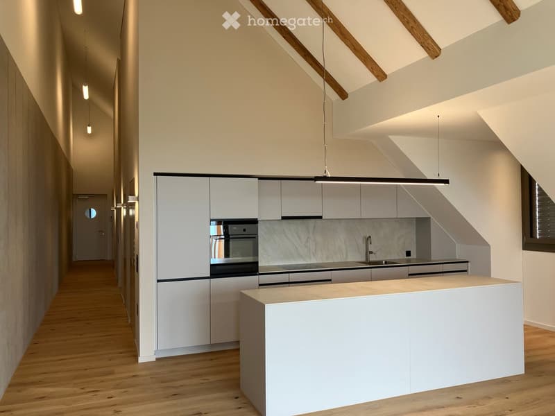 Modern kitchen with white cabinets, a central island, and built-in appliances, featuring wooden flooring and exposed wooden beams on the ceiling.