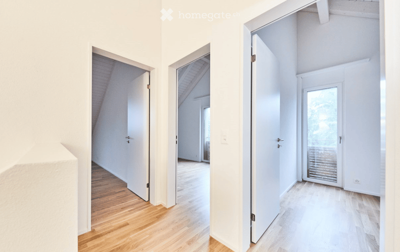 Bright, minimalist hallway with white walls, wooden flooring, and multiple open doors leading to other rooms.