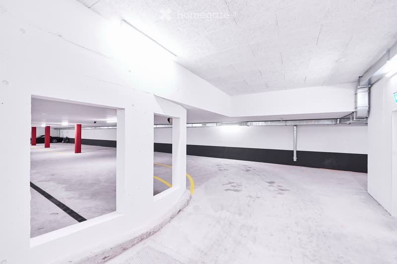Underground parking area with white walls, concrete floor, red support pillars, and yellow parking lines.