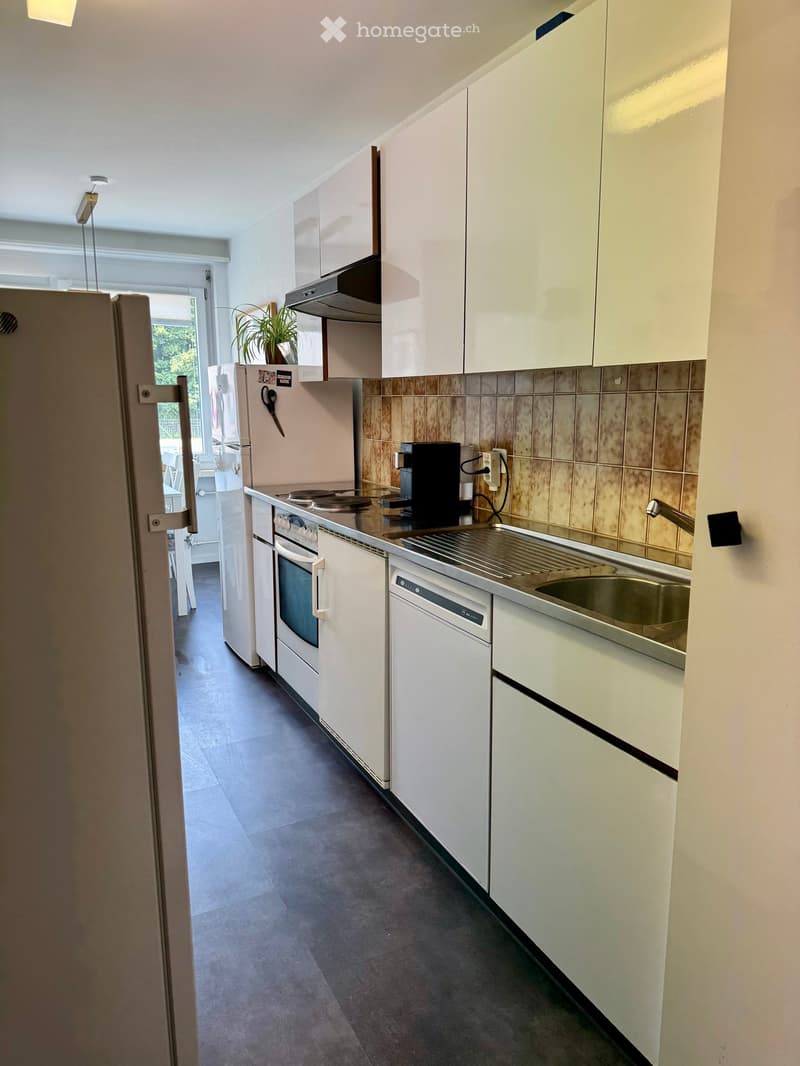 Modern kitchen with white cabinets, stainless steel appliances, and a dark tiled backsplash. Features a refrigerator, oven, dishwasher, coffee maker, and sink.