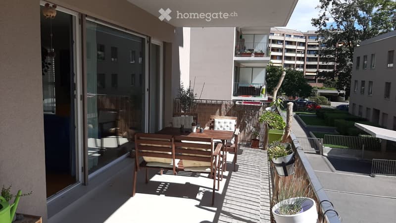Balcony with wooden furniture, potted plants, and a view of neighboring buildings.