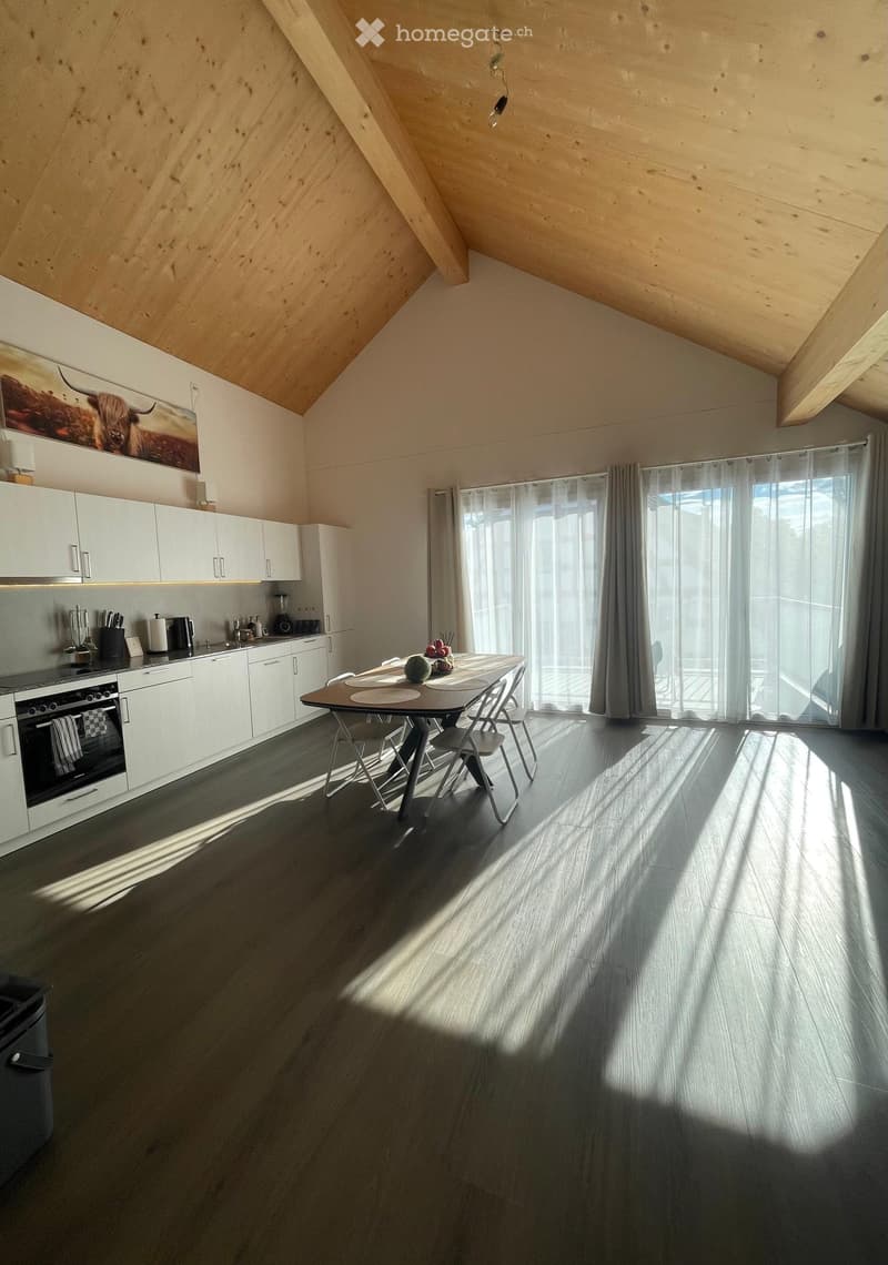 Modern kitchen with white cabinetry, stainless steel appliances, a dining table with chairs, and large windows with sheer curtains.
