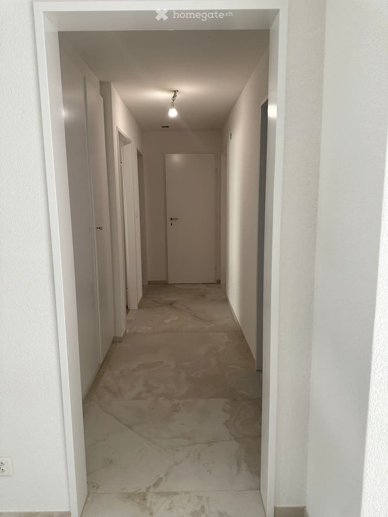 Empty hallway with white walls, tiled floor, and a single light fixture on the ceiling. Doors are visible on both sides.