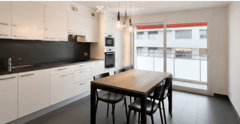Modern kitchen and dining area with white cabinets, black countertops, a wooden dining table with black chairs, and a large window overlooking a balcony.