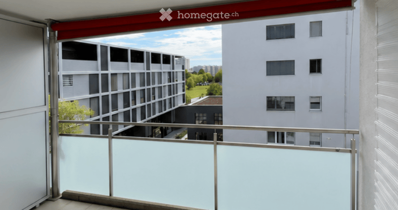 Balcony with a modern metal railing, overlooking a cityscape with contemporary buildings and greenery.