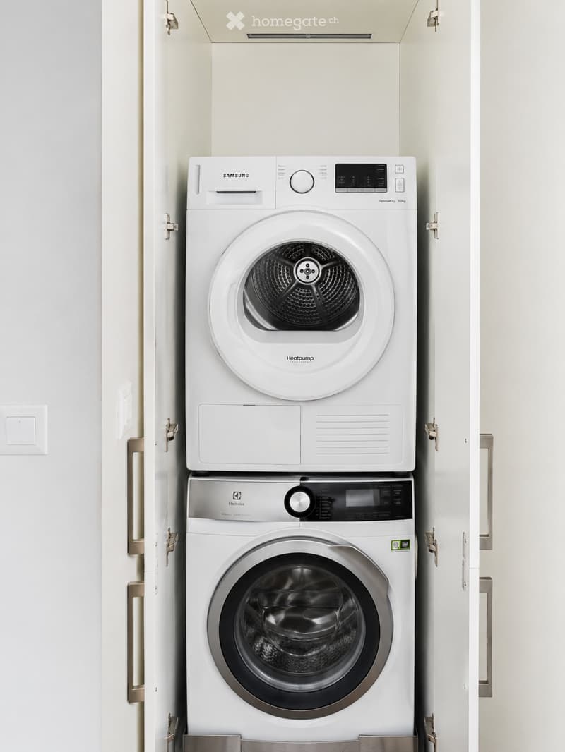 A compact bathroom with a stacked washing machine and dryer unit, both white with modern control panels.