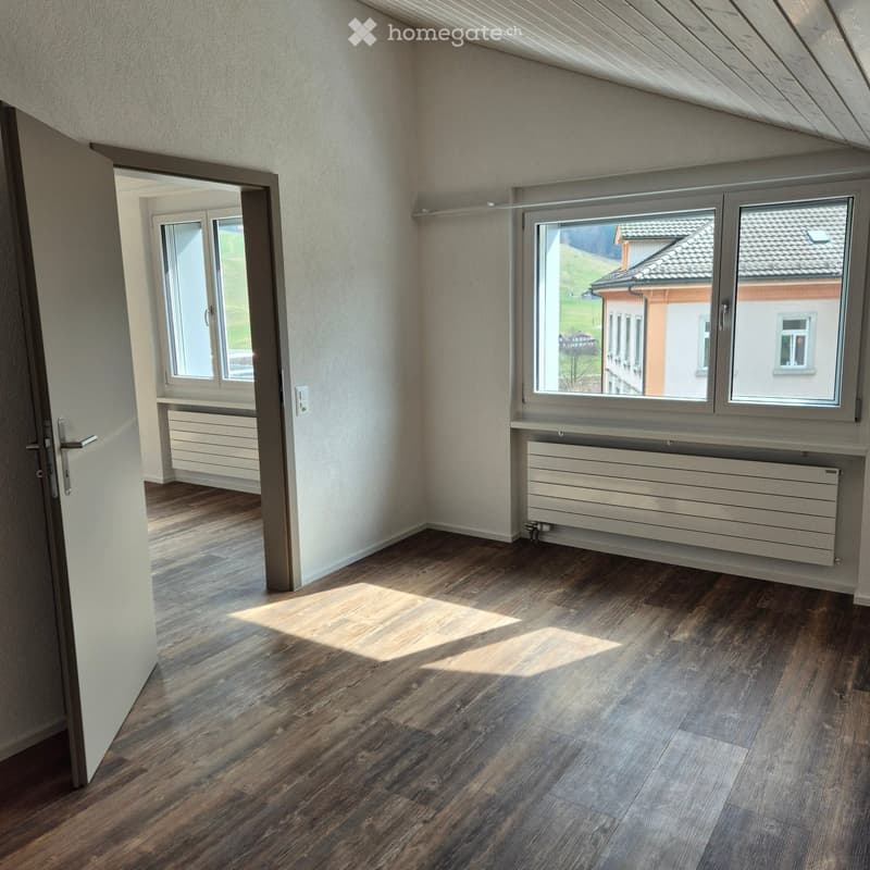 Empty room with wooden flooring, white walls, large windows, and radiators. No furniture or equipment present.