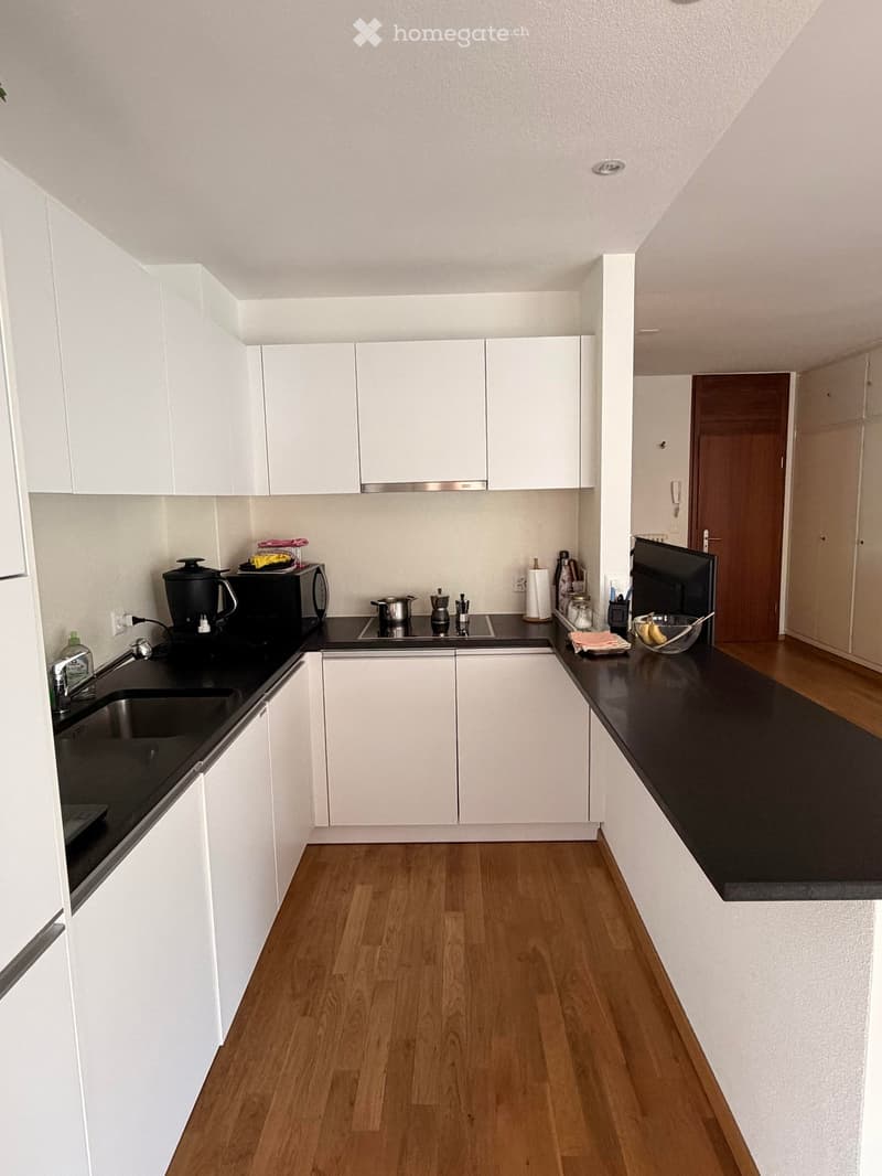 Modern kitchen with white cabinets, black countertops, wooden flooring, and various appliances including a coffee maker, microwave, and stove.