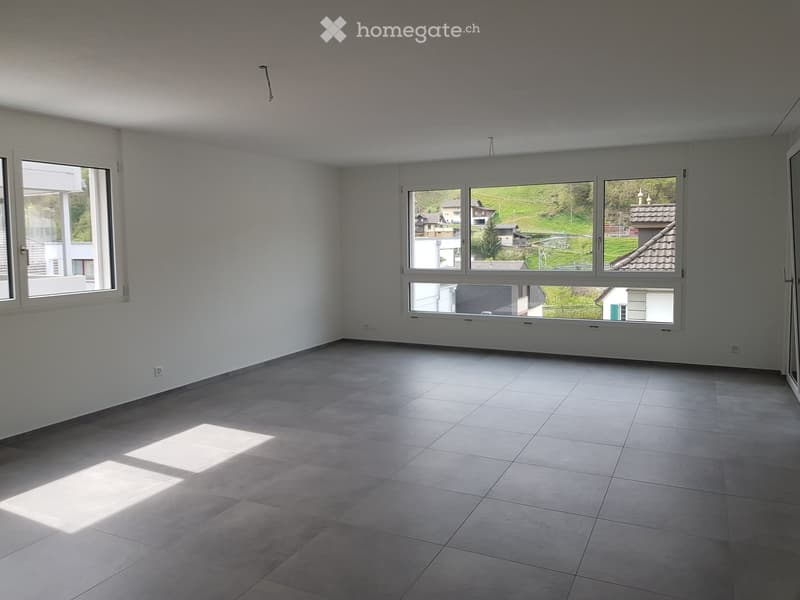 Empty room with gray tiled floor, white walls, two large windows with views of the exterior landscape