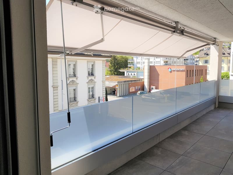 exterior view of a balcony with a metal railing and a glass wall with a retractable shade