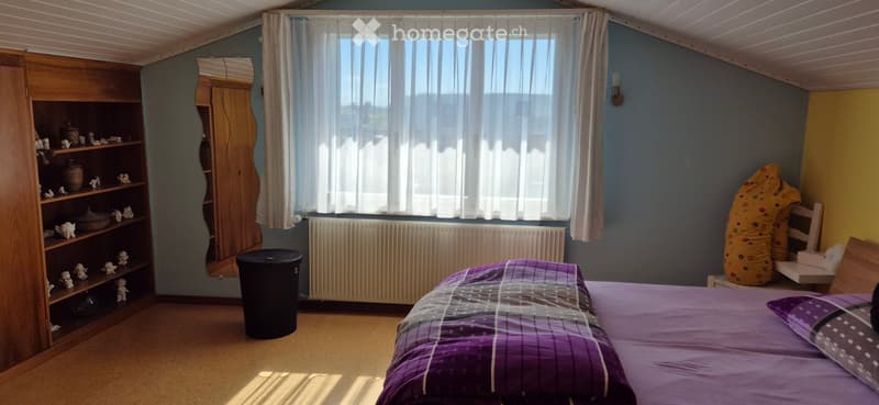 Cozy bedroom with a bed, wooden shelf, mirror, chair, and a large window with curtains.