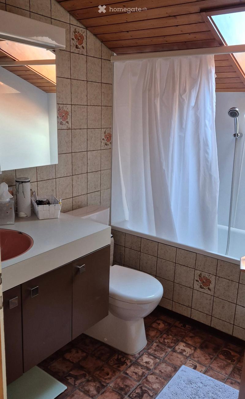Bathroom with a sink, toilet, bathtub, and shower curtain. Features tiled walls and a wooden slanted ceiling.