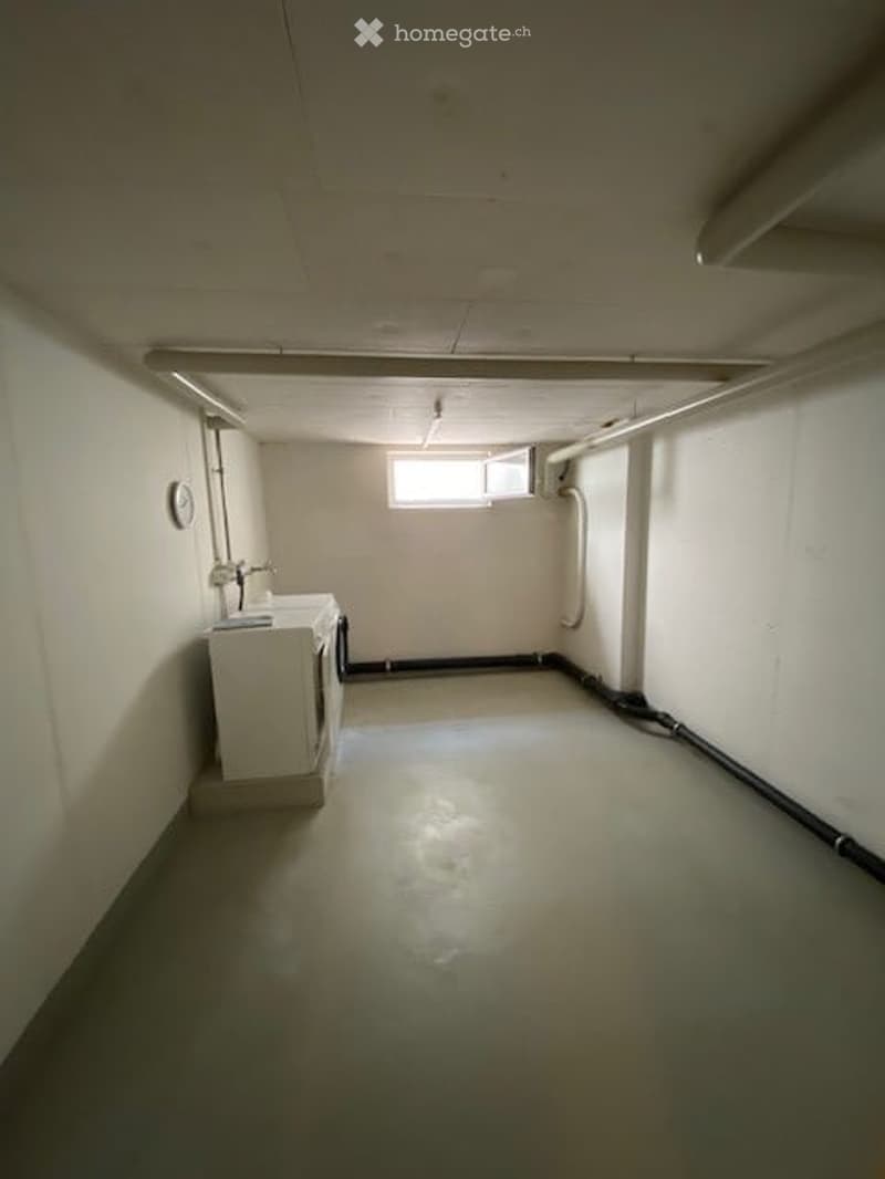 Empty room with a concrete floor, white walls, and a small window. There is a washing machine and a sink in the corner.
