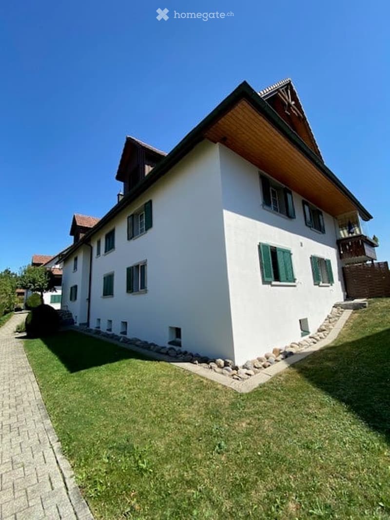 A two-story white house with green shutters, a wooden roof, and a well-maintained lawn.
