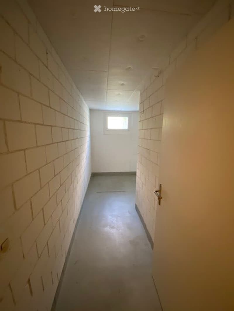 Empty hallway with white brick walls, a small window at the end, and a door on the right side.