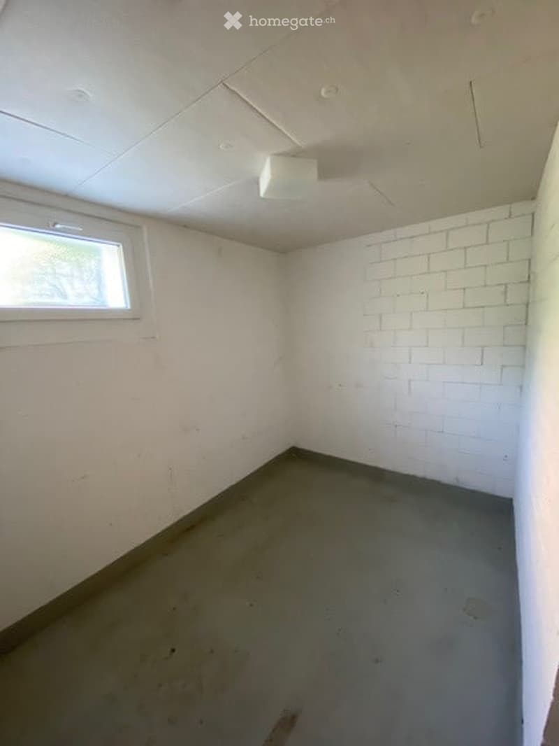 Empty room with white brick wall, concrete floor, and single window. No furniture or equipment present.