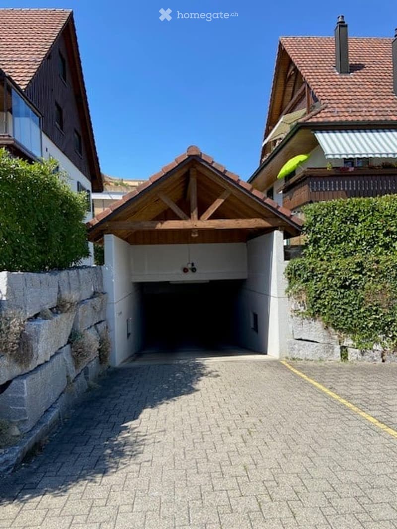 A modern garage with a wooden roof and stone walls, situated between two residential houses.