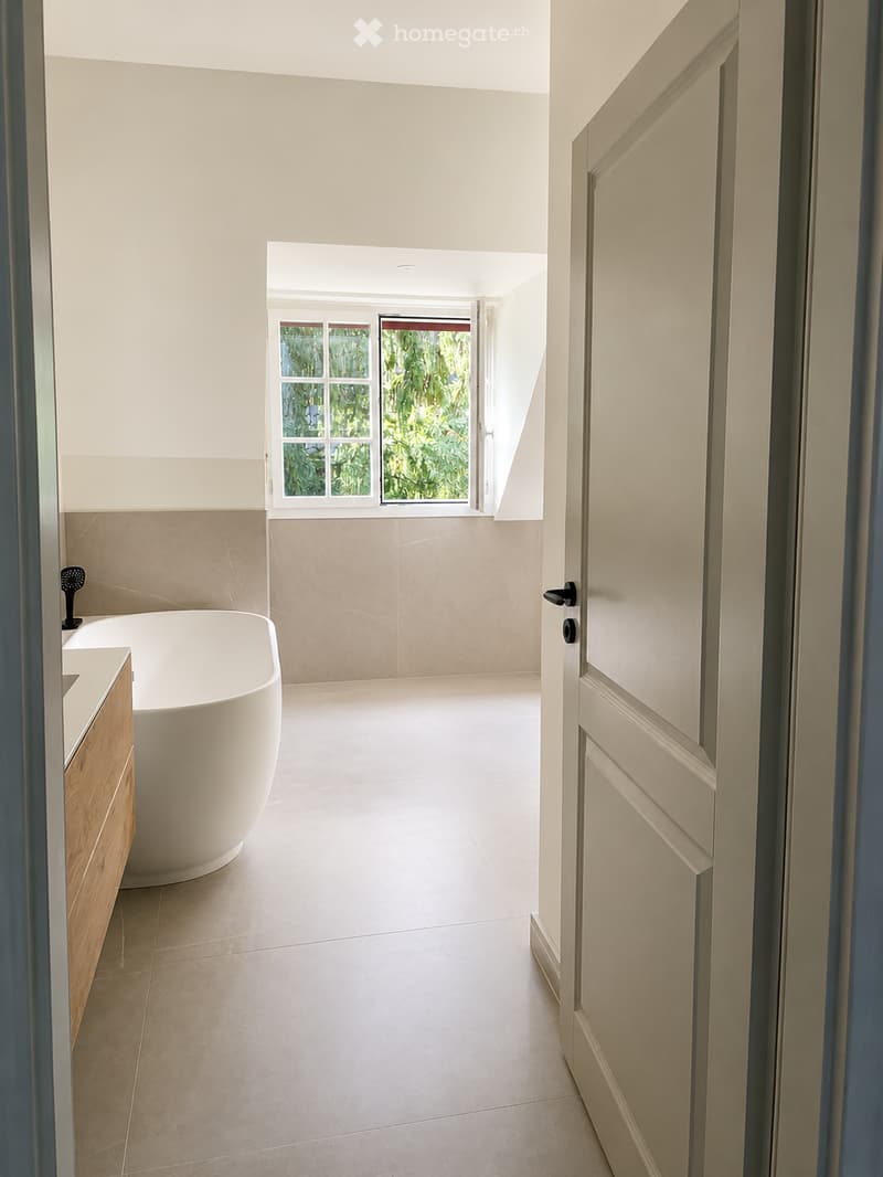 Modern bathroom with a freestanding bathtub, sleek wooden cabinet, and a large window offering a view of greenery.