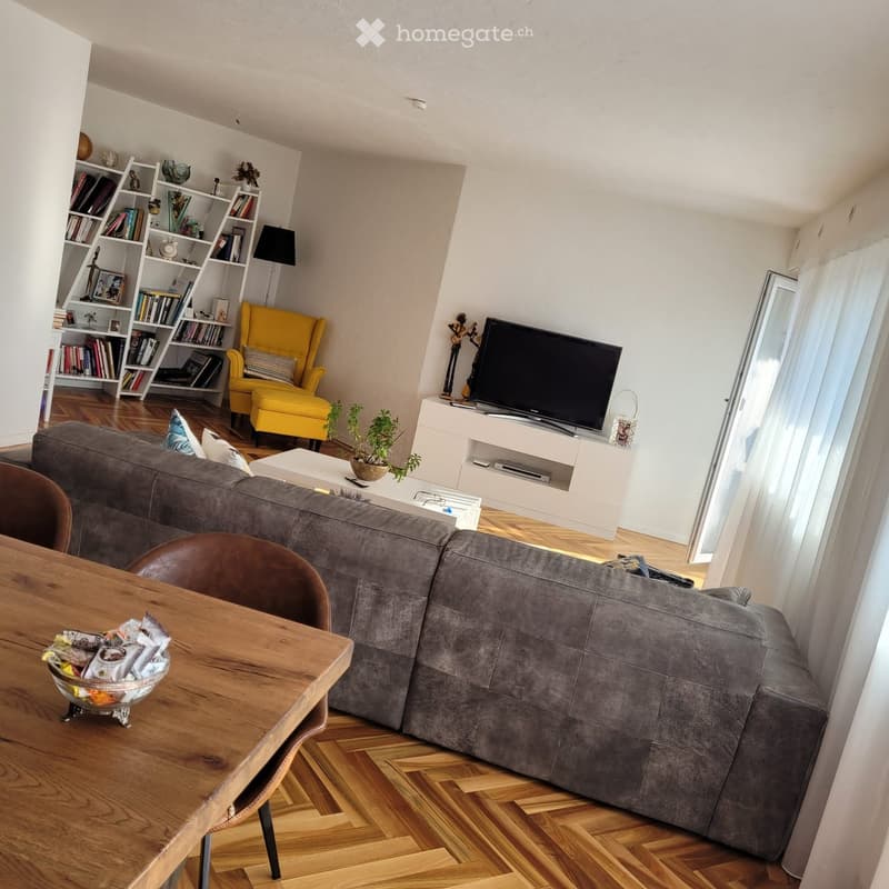 Modern living room with grey sectional sofa, wooden coffee table, yellow armchair, bookshelf, TV stand, and decorative items.