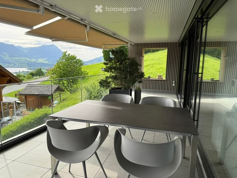 Balcony with a modern table and chairs, overlooking a scenic landscape with mountains and greenery.