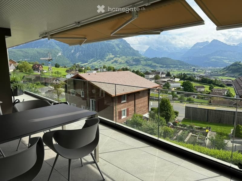 Balcony with a panoramic mountain view, featuring a modern table and chairs, glass railing, and retractable awning.