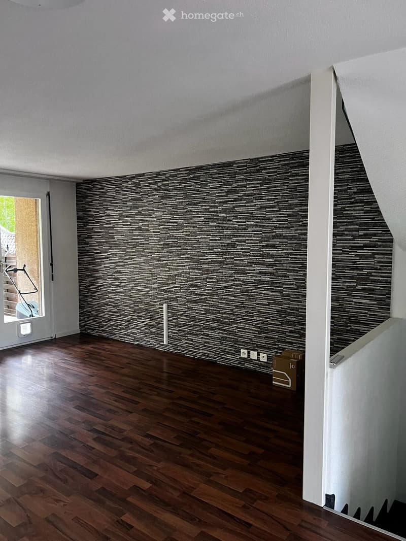 Empty room with wooden flooring and a textured wall design. The room features a white ceiling and a doorway leading to another space.