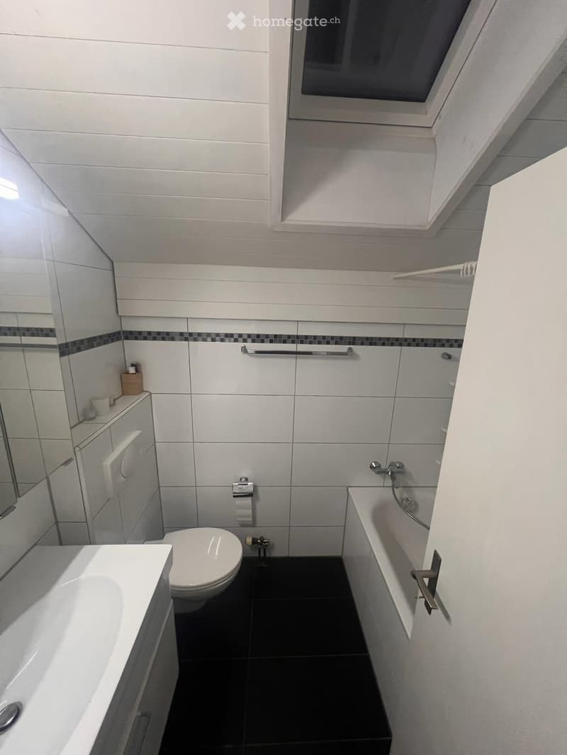 Modern bathroom with white tiles, black floor, bathtub, toilet, sink, mirror, and cabinet.