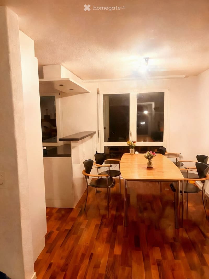 Dining area with wooden floor, dining table, chairs, and vase with flowers on the table.