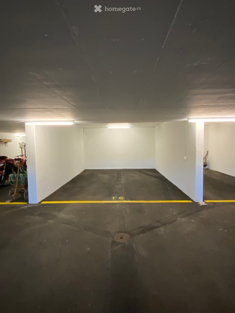 Empty underground parking space with marked parking spots, white walls, and a single motorcycle in the background.