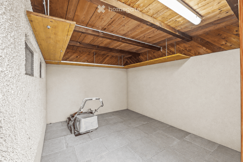 Empty room with a wooden ceiling, tiled floor, and a small window. A vacuum cleaner is placed in the corner.