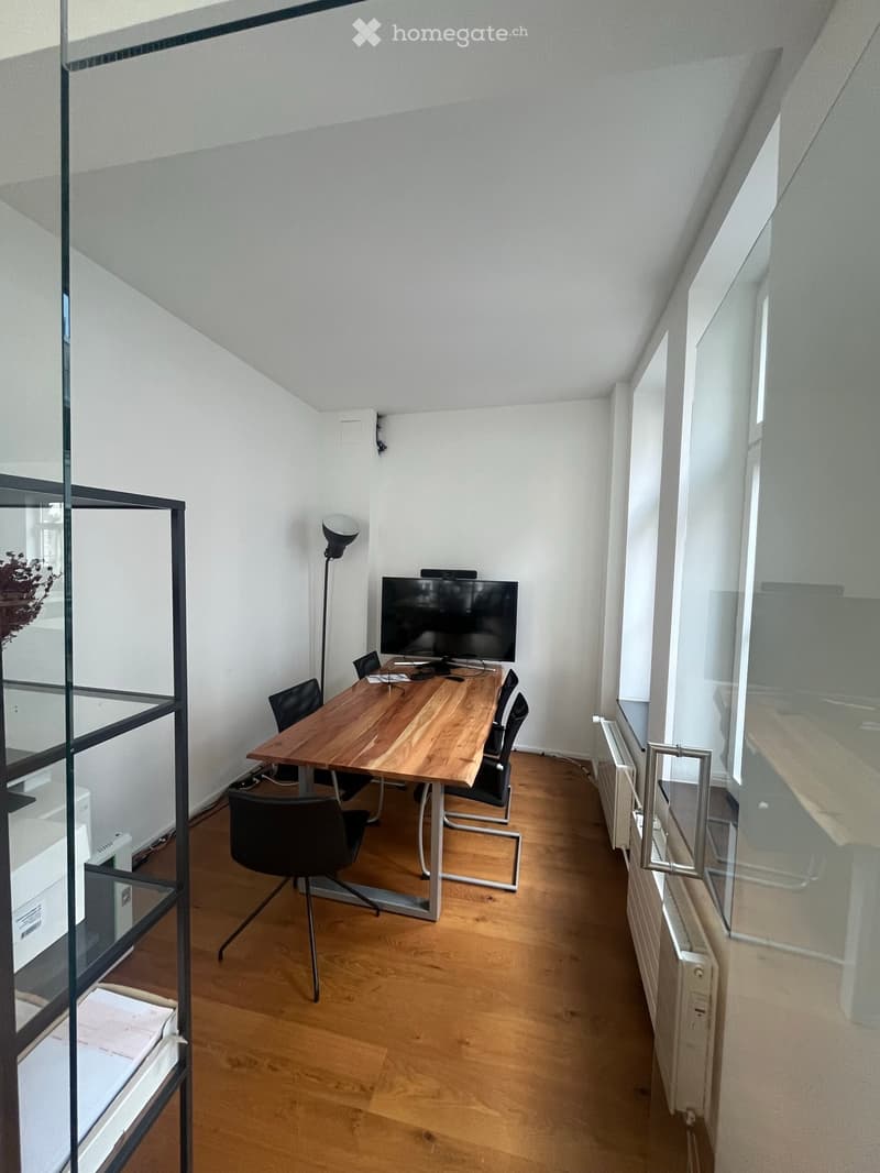 Modern office space with wooden floor, large glass windows, wooden table, chairs, screen, shelf, and lamp.