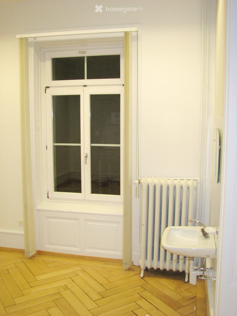 Bathroom with wooden floor, white walls, radiator, and sink.