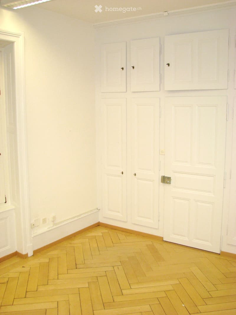 Empty room with white walls, wooden herringbone floor, and multiple white doors.
