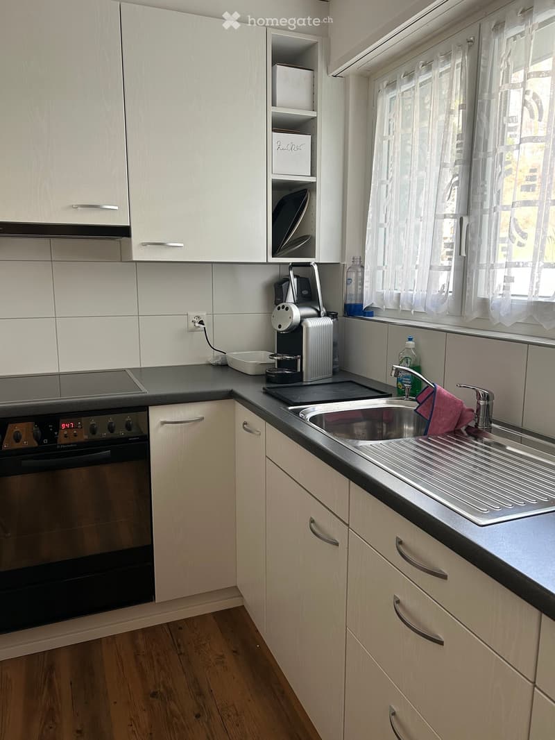 modern kitchen with white cabinets, black countertops, sink, stove, coffee maker, tiled walls, large window