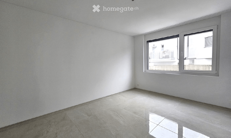 Empty room with white walls, tiled floor, and large windows offering a view of a neighboring building and balcony.
