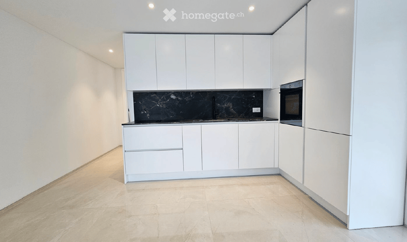 Modern kitchen with white cabinets, black countertop, and built-in oven. Light-colored tiled floor.